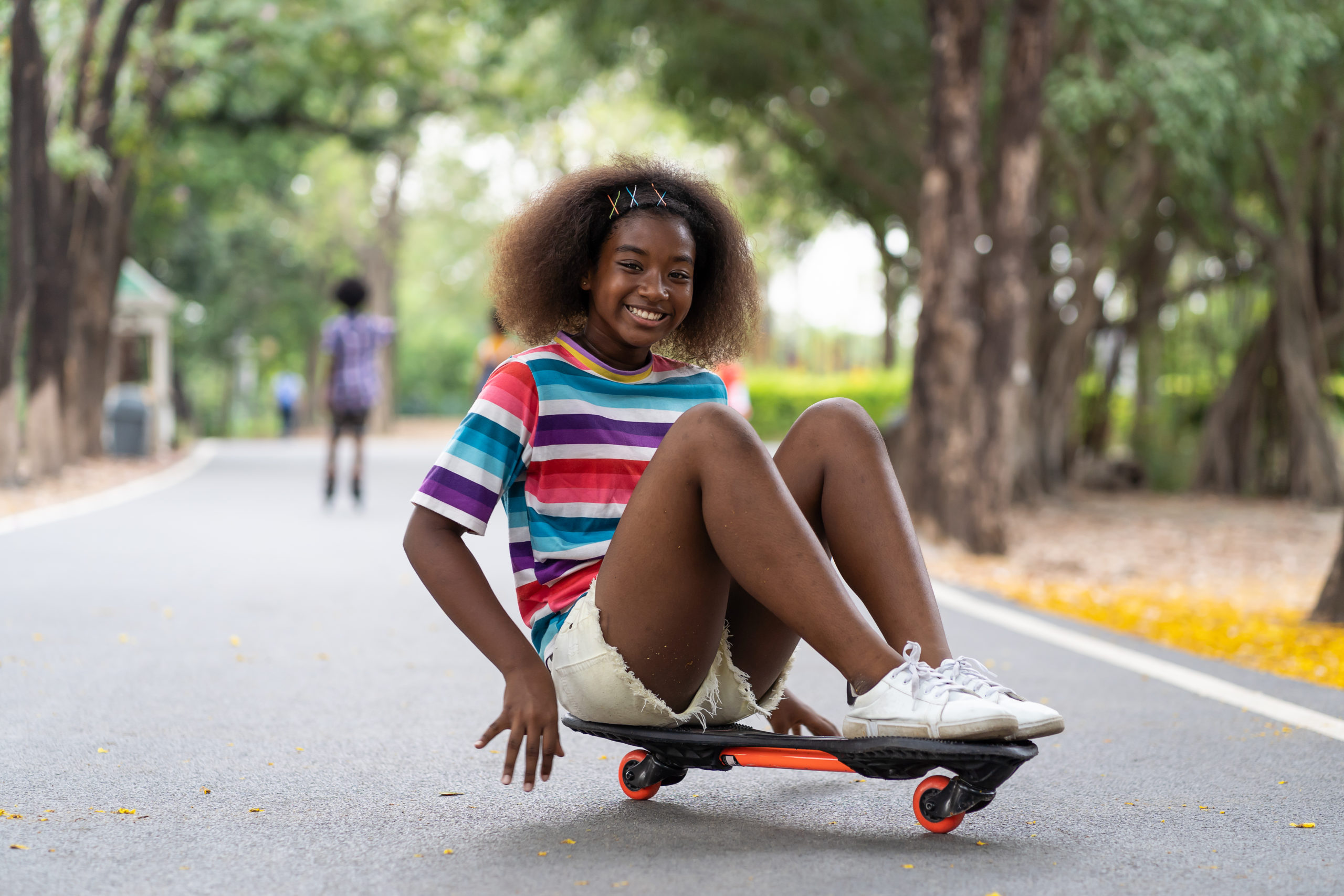Happy young girl playing on the skateboard in the park. African American girl with curly hair practicing skateboard